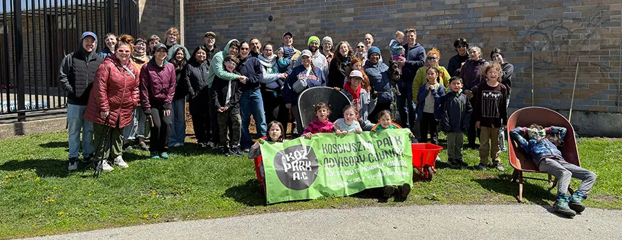 Group photo of about forty adults and children on the grass in front of a brick building, with wheelbarrows and a green banner reading Koz Park A.C., Kosciuszko Park Advisory Council.